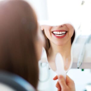 A young female admires her new smile in the mirror after completing professional teeth whitening treamtent