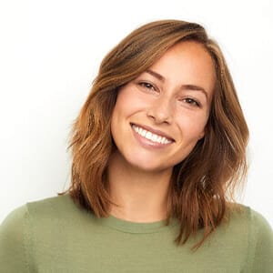 A young female is wearing a green blouse and smiling after having her teeth whitened