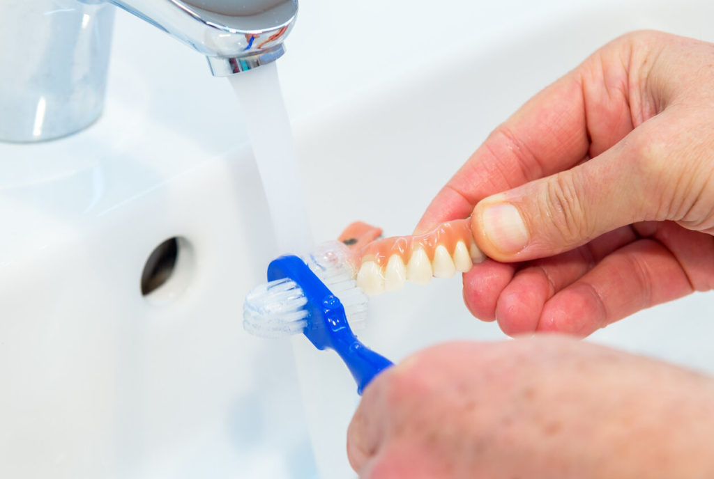 person cleaning dentures in Greensboro with toothbrush