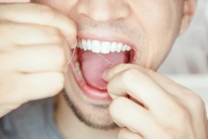 Closeup of a man flossing his dental implants.