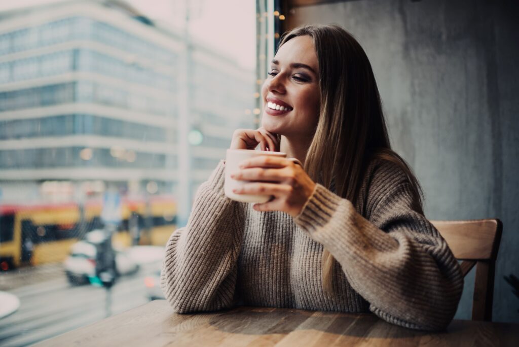 Woman holding coffee mug looking out window smiling