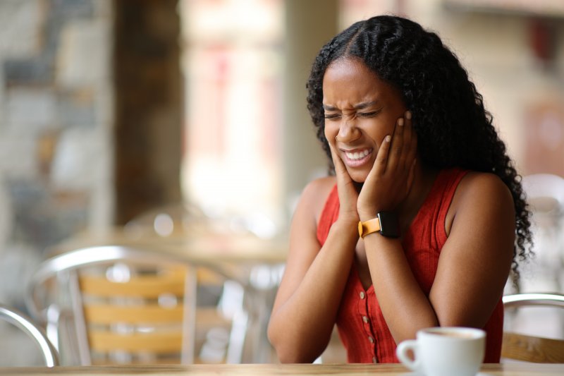 A woman suffering from TMJ disorder in a restaurant setting