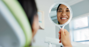 a woman in a dental office looking at her smile in a handheld mirror